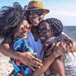 Three friends enjoying a sunny day at the beach, embracing with smiles.